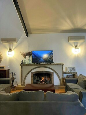 A living room with a fireplace, a television mounted above it, and two wall-mounted air conditioners. - Private retreat with pool near Seville (Utrera)
