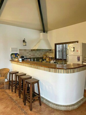 A kitchen with a bar area, a stove, a refrigerator, and a window with blinds. - Private retreat with pool near Seville (Utrera)