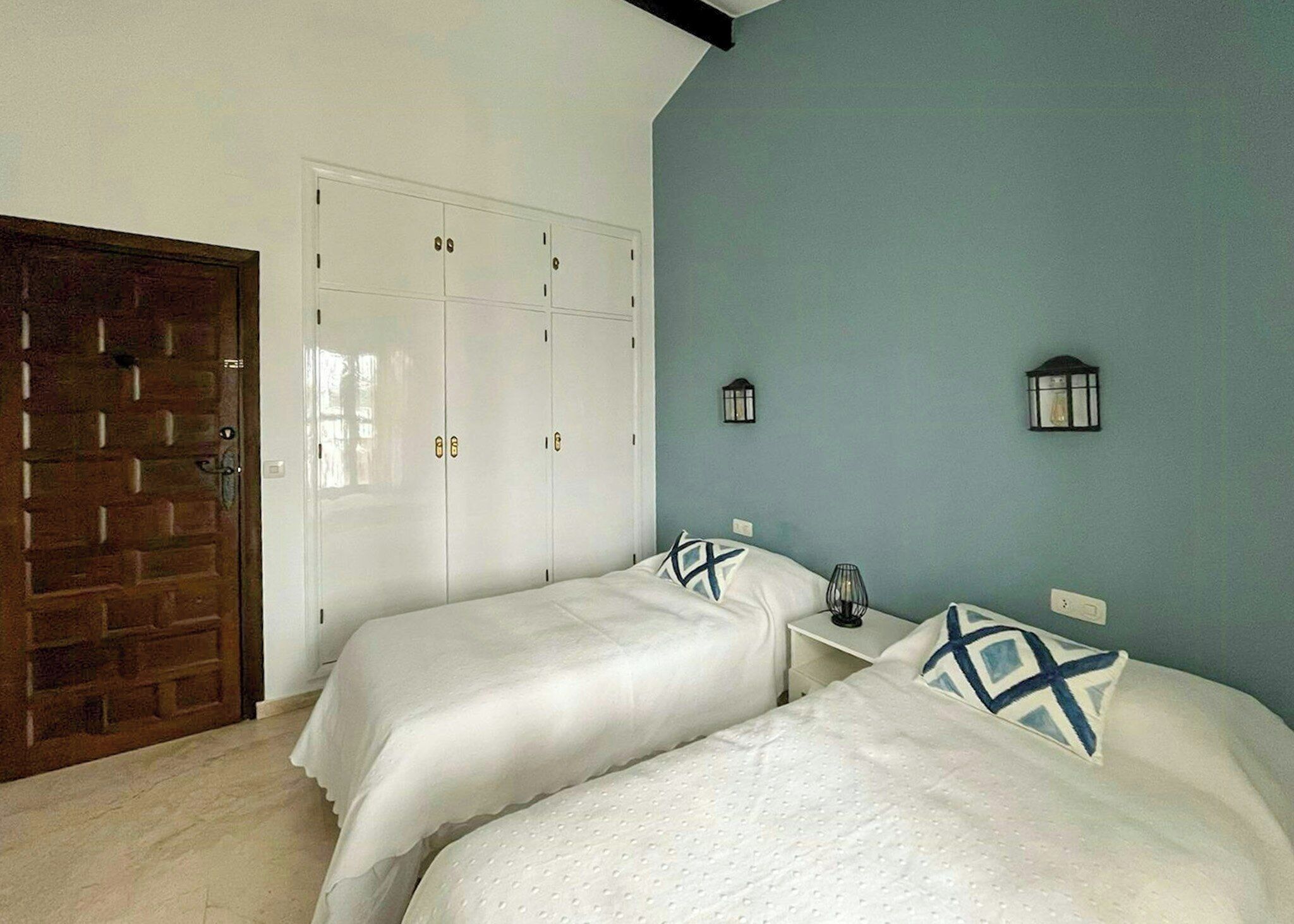 A bedroom with two beds, a wardrobe, and a brick wall.