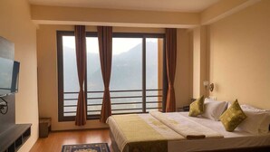 Une chambre d’hôtel avec un lit, une télévision, une fenêtre avec des rideaux et une vue sur les montagnes.