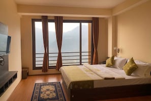 Una habitación de hotel con una cama, televisión, ventana con cortinas y vistas a las montañas.