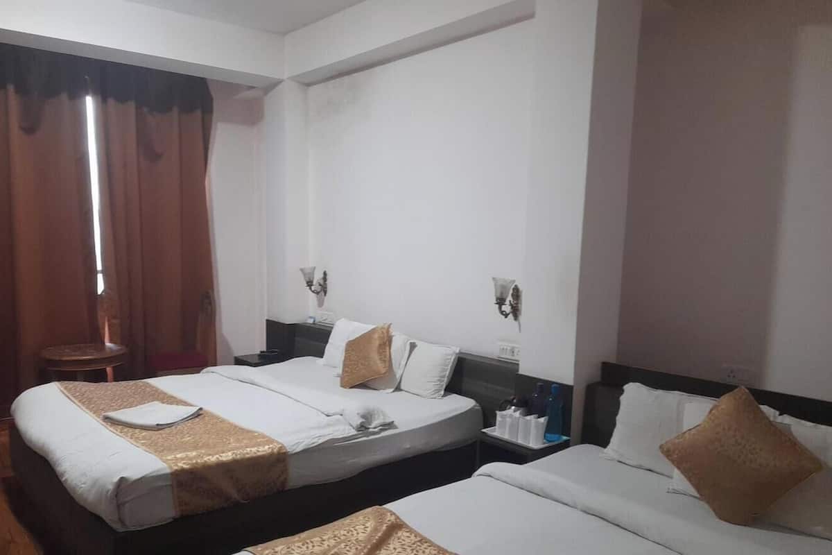 Habitación de hotel con dos camas, una mesita, una lámpara y un ventanal con cortinas.