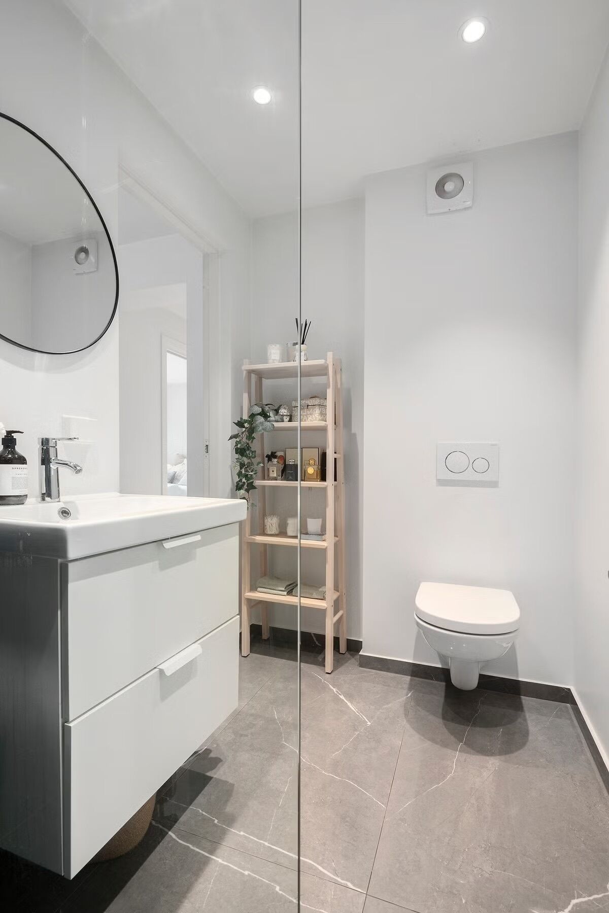 A modern bathroom with a white vanity, a mirror, a toilet, and a wooden shelf unit.