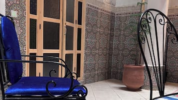 Une pièce comprenant un fauteuil bleu rembourré, une chaise en métal, un meuble en bois doté de portes en verre, des carreaux décorés et une plante en pot.