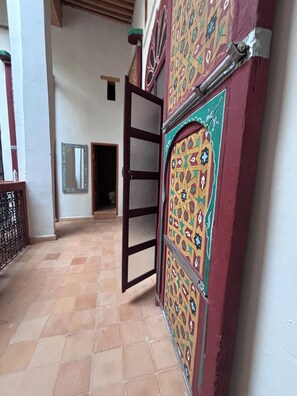 Un couloir au sol carrelé, une porte ornée de motifs complexes et un miroir accroché au mur.