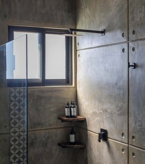 Ein Badezimmer mit einem großen Fenster, einer Dusche mit Regendusche und zwei Ablagen für Toilettenartikel.