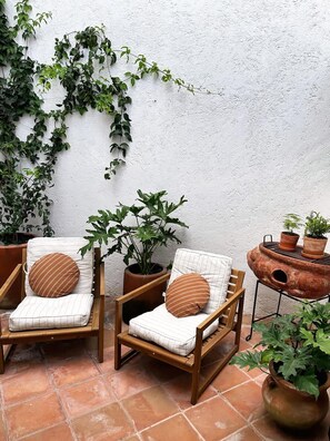 Zwei Holzstühle mit gestreiften Kissen und runden Polstern, ein Blumentopf und ein Terrakottatopf auf einer gefliesten Terrasse.