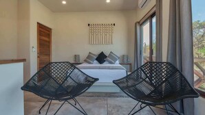 Un dormitorio con cama, dos sillas negras, una ventana con cortinas y un equipo de aire acondicionado instalado en la pared.