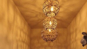 Una habitación con escalera de madera, lámpara de techo tejida y un cuadro en la pared.