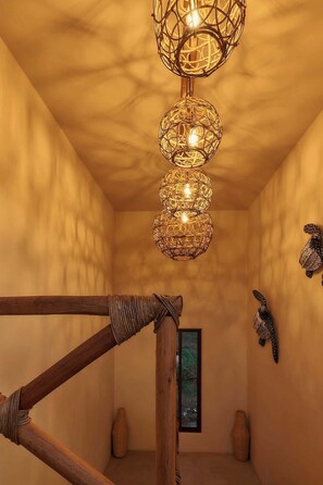 Ein Zimmer mit einer Holztreppe, einer gewebten Deckenleuchte und einem gerahmten Kunstwerk an der Wand.