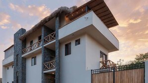Un edificio moderno de varios pisos con techo plano, balcones y entrada protegida por una verja.