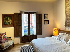 Ein Schlafzimmer mit Bett, Stuhl, Fenster mit Rollläden und einer Lampe.