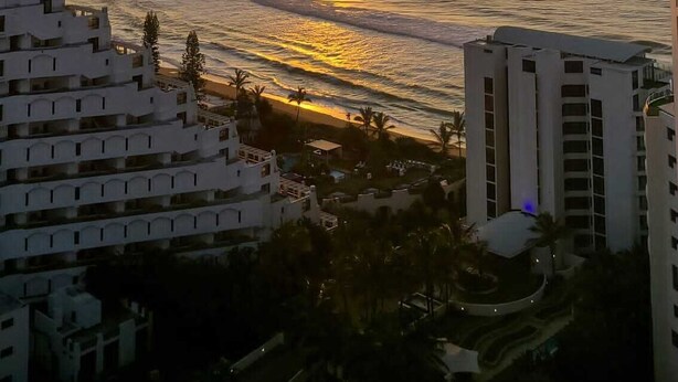 A coastal view with a sunset, buildings, and a clear sky.