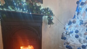 A fireplace with a lit fire, a Christmas tree with blue ornaments, and a doormat with a Christmas tree design.