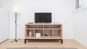 A minimalist room with a television on a wooden stand, a floor lamp, and a small table with a vase and a remote control.