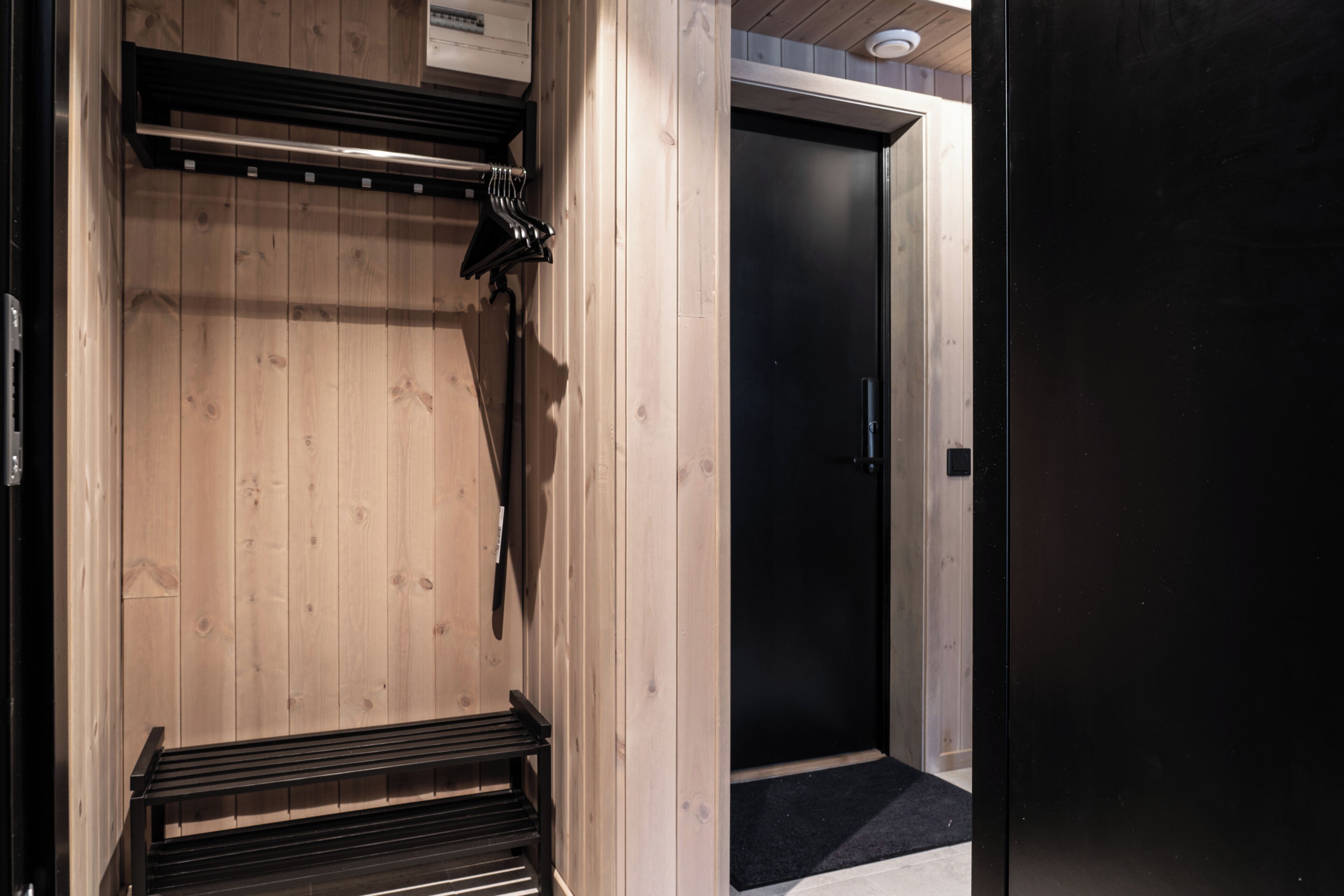 A wooden interior with a bench, a coat rack, and a door.
