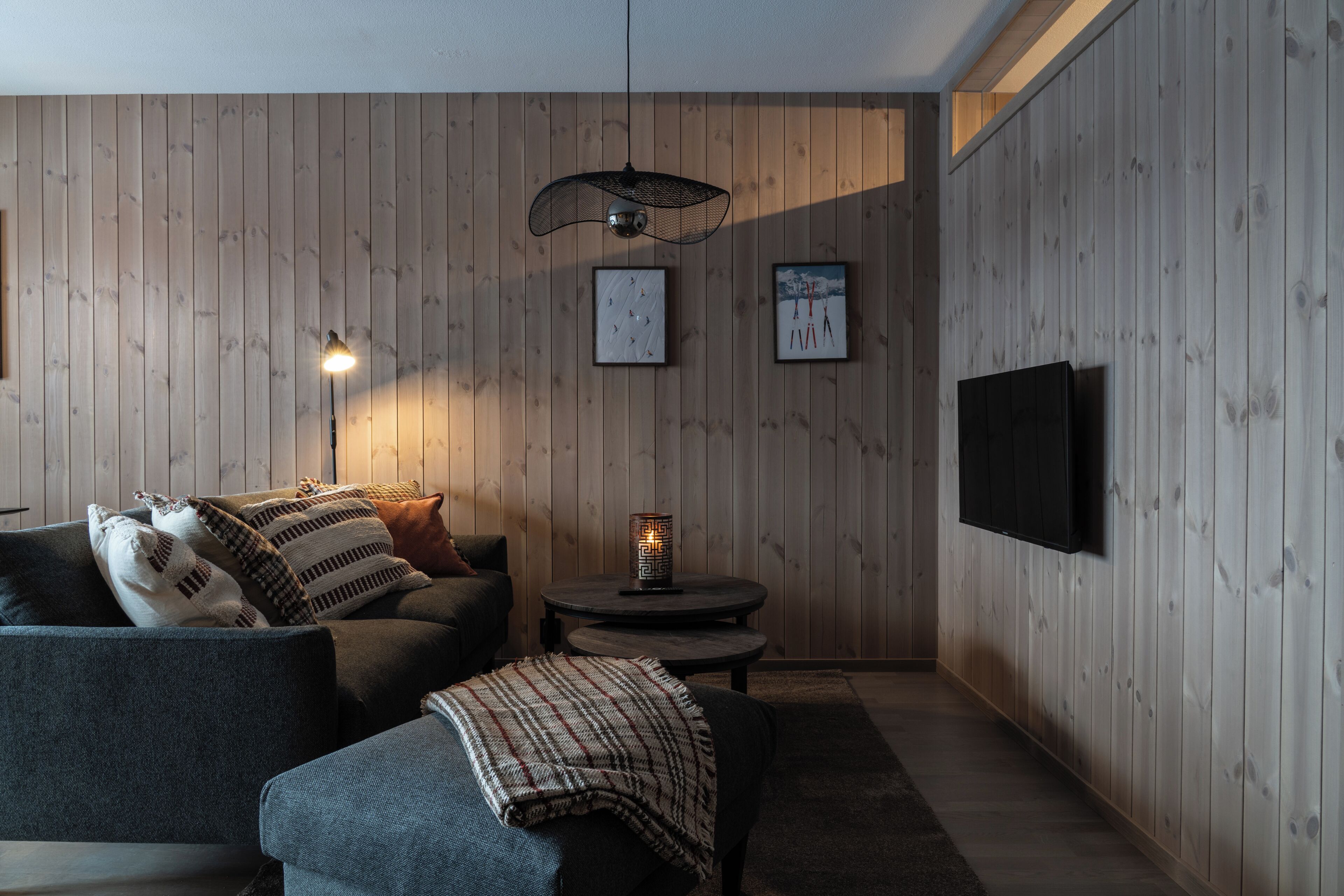 Une pièce confortable avec un canapé, une petite table avec une lampe et un téléviseur fixé au mur.