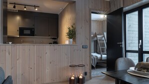Una cocina moderna con paneles de madera, un microondas y una planta. Hay una zona de comedor con una mesa y sillas.