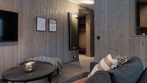 Una sala moderna con paneles de madera, un televisor de pantalla plana, una mesa redonda y un sofá gris con cojines estampados.