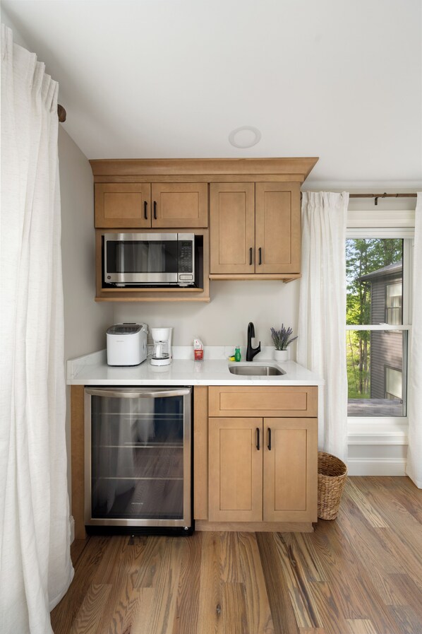A compact kitchen with wooden cabinets, a built-in microwave, a coffee maker, and a refrigerator.