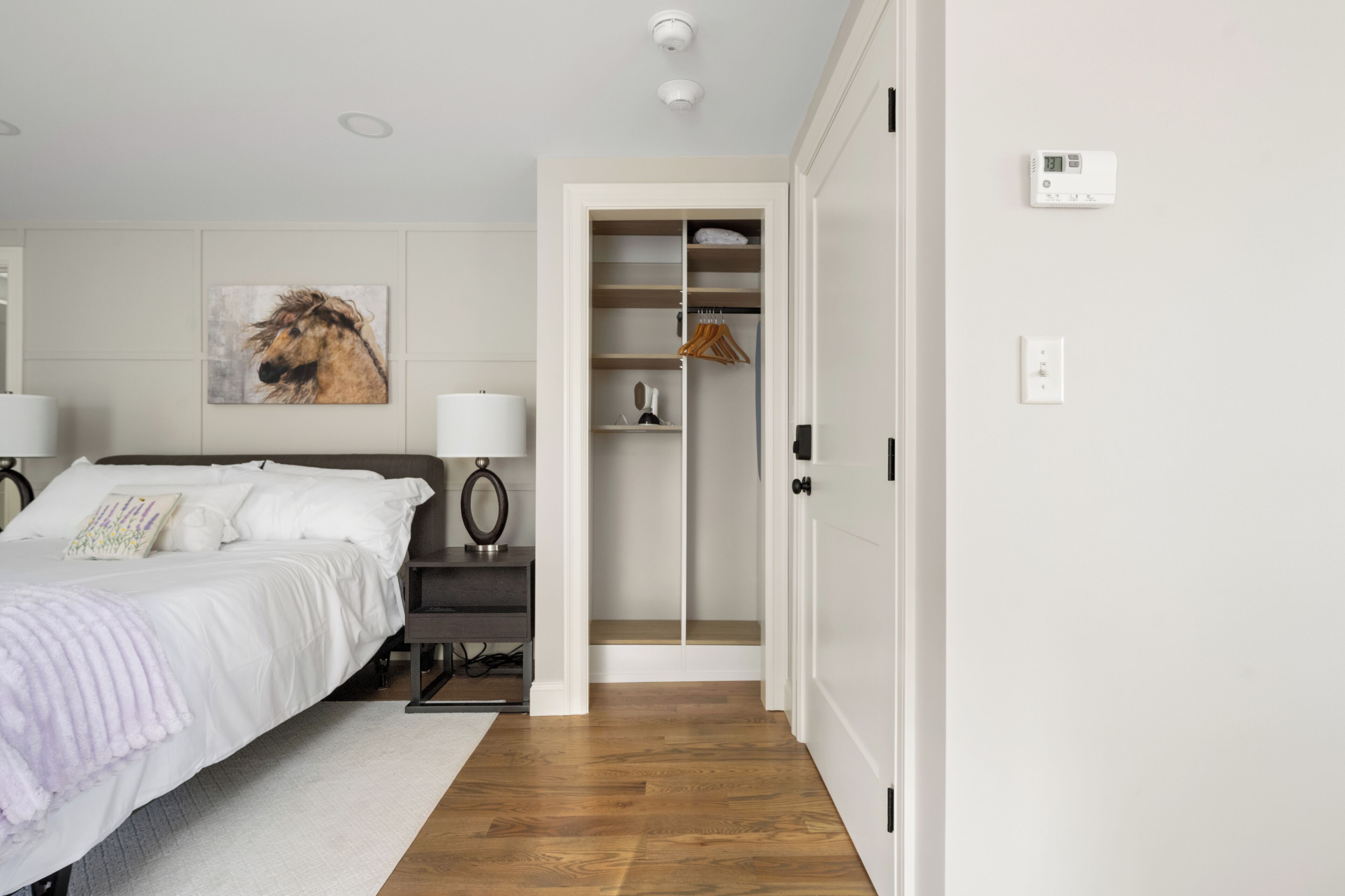 Une chambre à coucher comprenant un lit, des lampes de chevet, une table de chevet, une armoire et un thermostat fixé au mur.