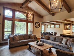 A spacious living room with large windows, a sectional sofa, a coffee table, and a dining area with chairs. - Gorgeous Mountain Escape with Access to Exclusive Golf (Sunriver)