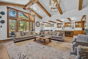 A spacious living room with a large sectional sofa, a wooden coffee table, and a dining area with a kitchen in the background. - Gorgeous Mountain Escape with Access to Exclusive Golf (Sunriver)