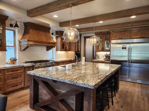 A kitchen with wooden cabinets, a stainless steel refrigerator, granite countertops, and pendant lighting. - Gorgeous Mountain Escape with Access to Exclusive Golf (Sunriver)