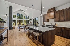 A spacious kitchen with a large island, wooden cabinets, and a view of the outdoors. - Beautiful Forest Escape with Access to Forest House (Sunriver)