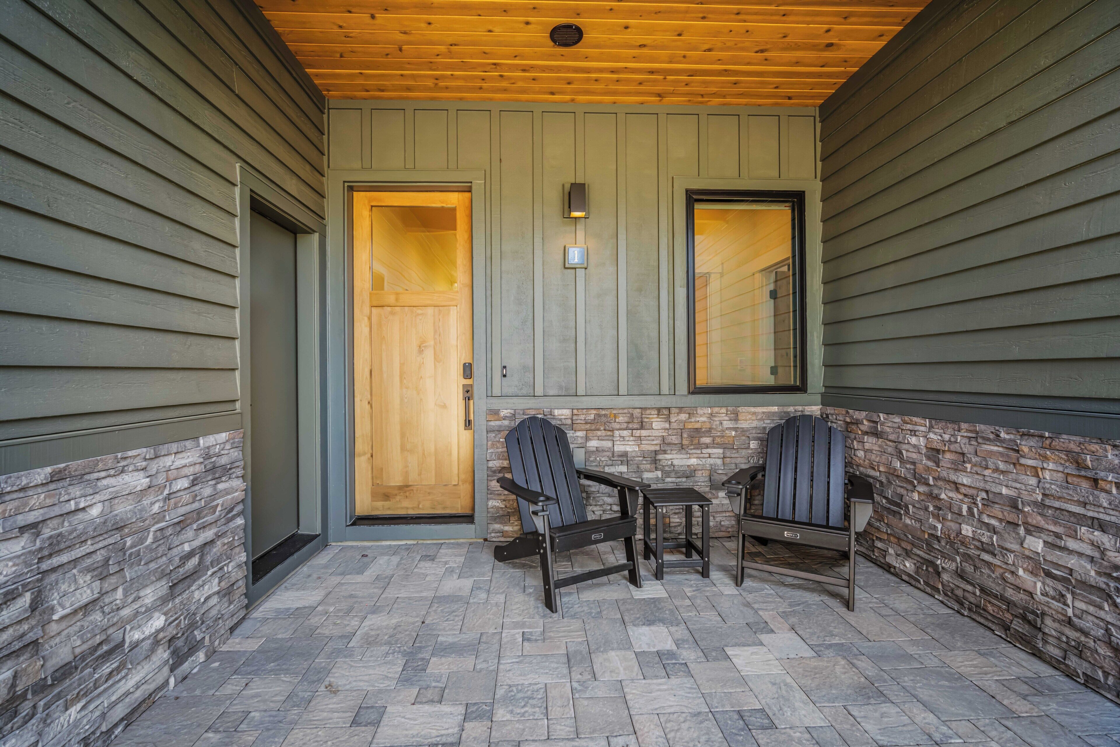 Un portico coperto con due poltrone Adirondack, un tavolino e una porta in legno.