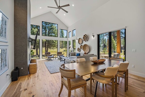 Un vaste espace de vie comprenant une grande table à manger en bois, des sièges confortables et de grandes fenêtres offrant une vue sur l’extérieur.