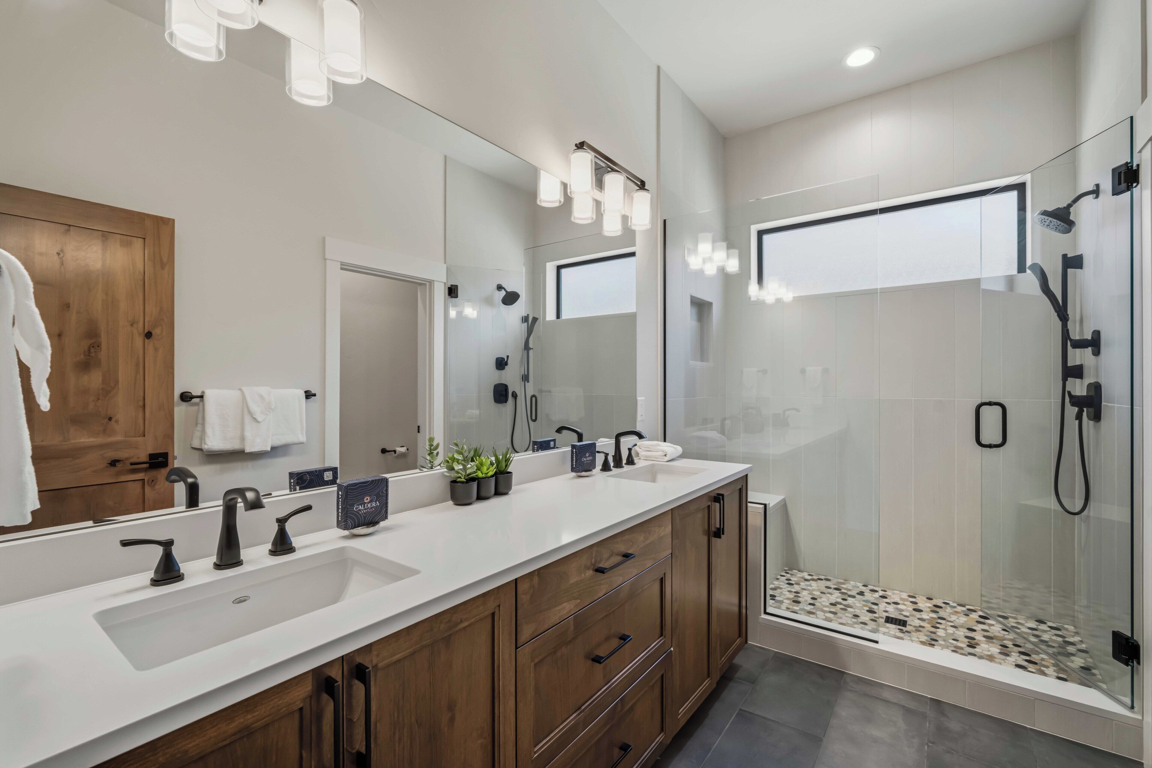 Une salle de bain moderne avec un grand miroir, deux vasques, des meubles en bois et une douche à parois de verre.