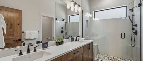 Une salle de bain moderne avec un grand miroir, deux vasques, des meubles en bois et une douche à parois de verre.