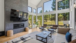 Ein modernes Wohnzimmer mit Kamin, großen Fenstern und Blick ins Freie.