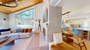 A modern living room with a sofa, a fireplace, and a dining area with a table and chairs. - Luxurious Sunriver Home with Access to Exclusive Golf (Sunriver)