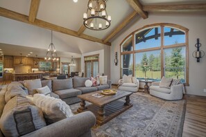 A spacious living area with a large sectional sofa, a coffee table, and a view of the kitchen and outdoors. - 56936 Dancing Rock Loop (Sunriver)