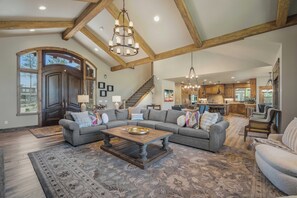 A spacious living room with a large sectional sofa, a wooden coffee table, and a staircase leading to an upper level. - 56936 Dancing Rock Loop (Sunriver)