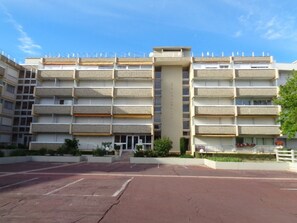 A multi-story building with a central vertical structure, balconies on each floor, and a parking area in front. - T2 Apartment with South Terrace - Beach Access (Arcachon)