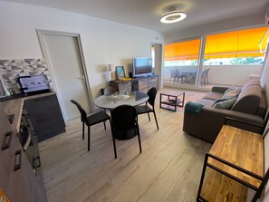 A modern living room with a sofa, a dining table with chairs, a TV, and a balcony with a view. - T2 Apartment with South Terrace - Beach Access (Arcachon)