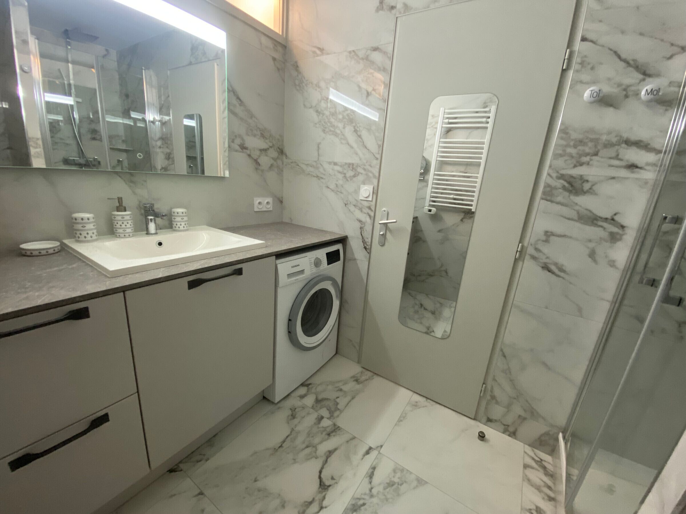 Une salle de bain équipée d’un lavabo, d’un lave-linge, d’un miroir et d’une douche.