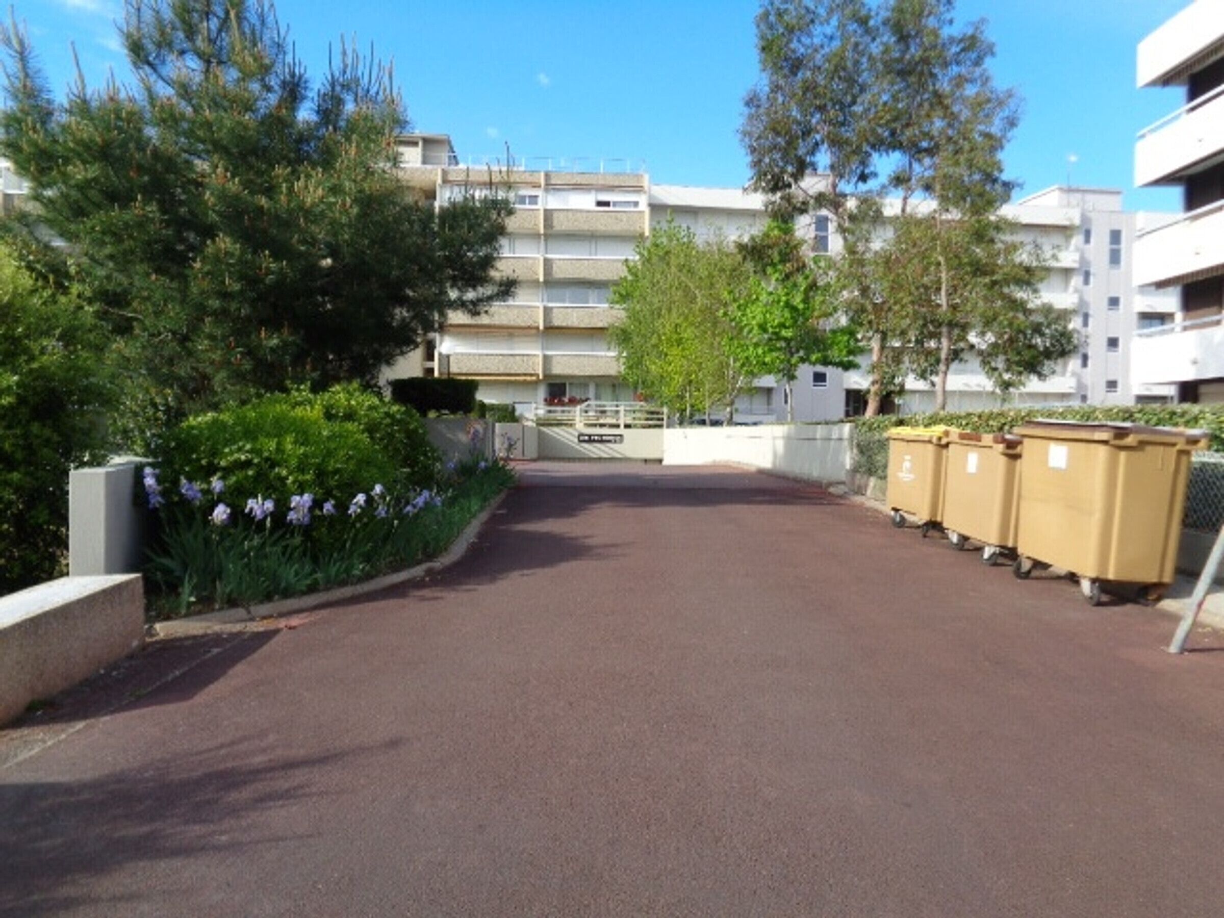 Un espace de stationnement avec une route asphaltée menant à un immeuble à plusieurs étages doté de balcons.