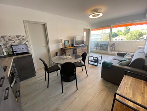 A modern apartment with a dining area, a sofa, a TV, and a balcony with a view. - T2 Apartment with South Terrace - Beach Access (Arcachon)
