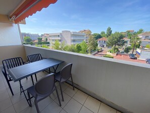 Un balcón con mesa y sillas, con vista a una zona residencial con casas y un estacionamiento.