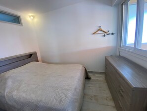 Un dormitorio con cama, cómoda, ventana y lámpara de pared.