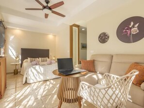 Een slaapkamer met een bed, een laptop op een tafeltje, een bank en een plafondventilator.