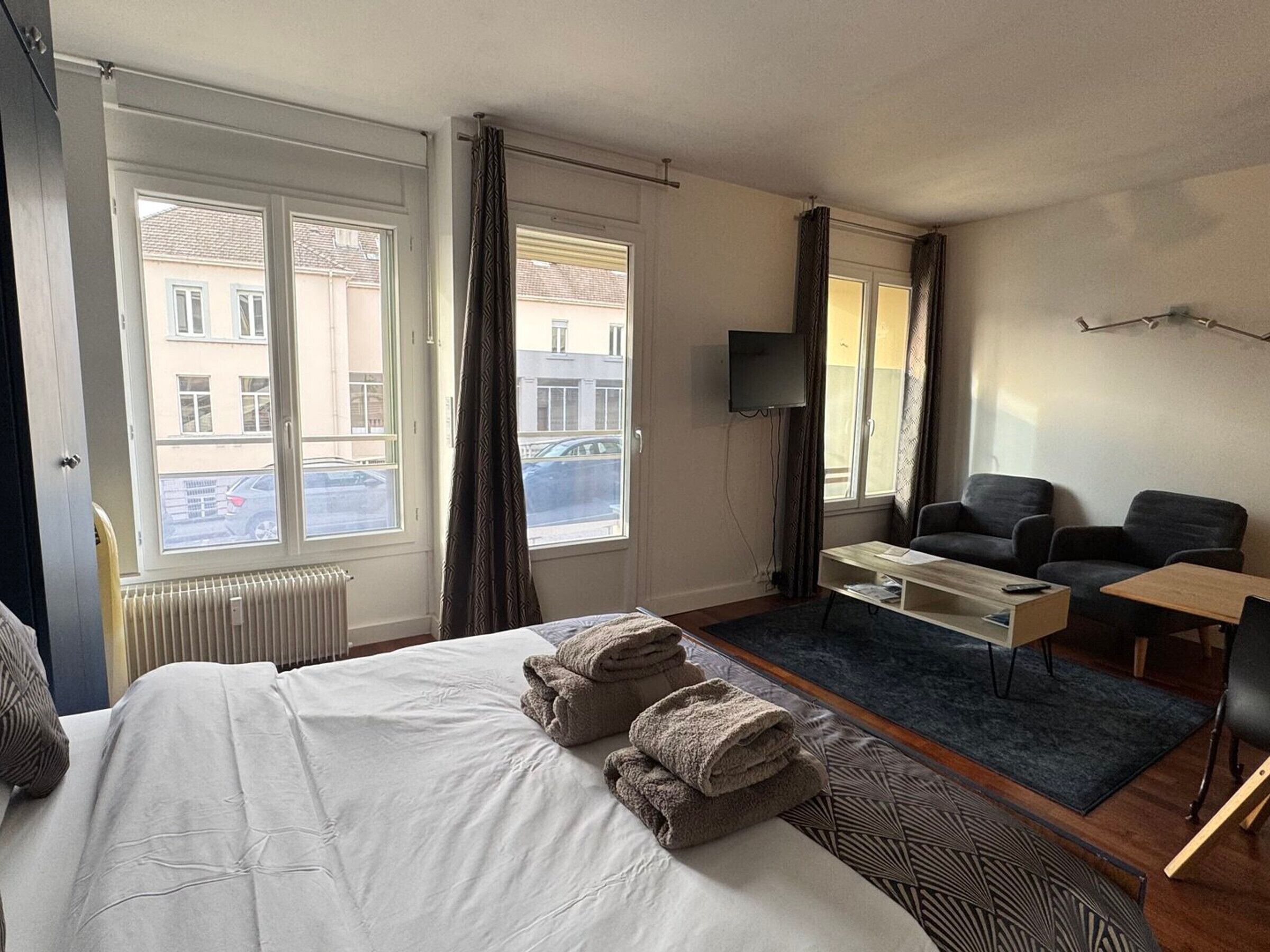 Une chambre d’hôtel équipée d’un lit, d’un bureau, d’une chaise, d’une télévision et de grandes fenêtres avec des rideaux.
