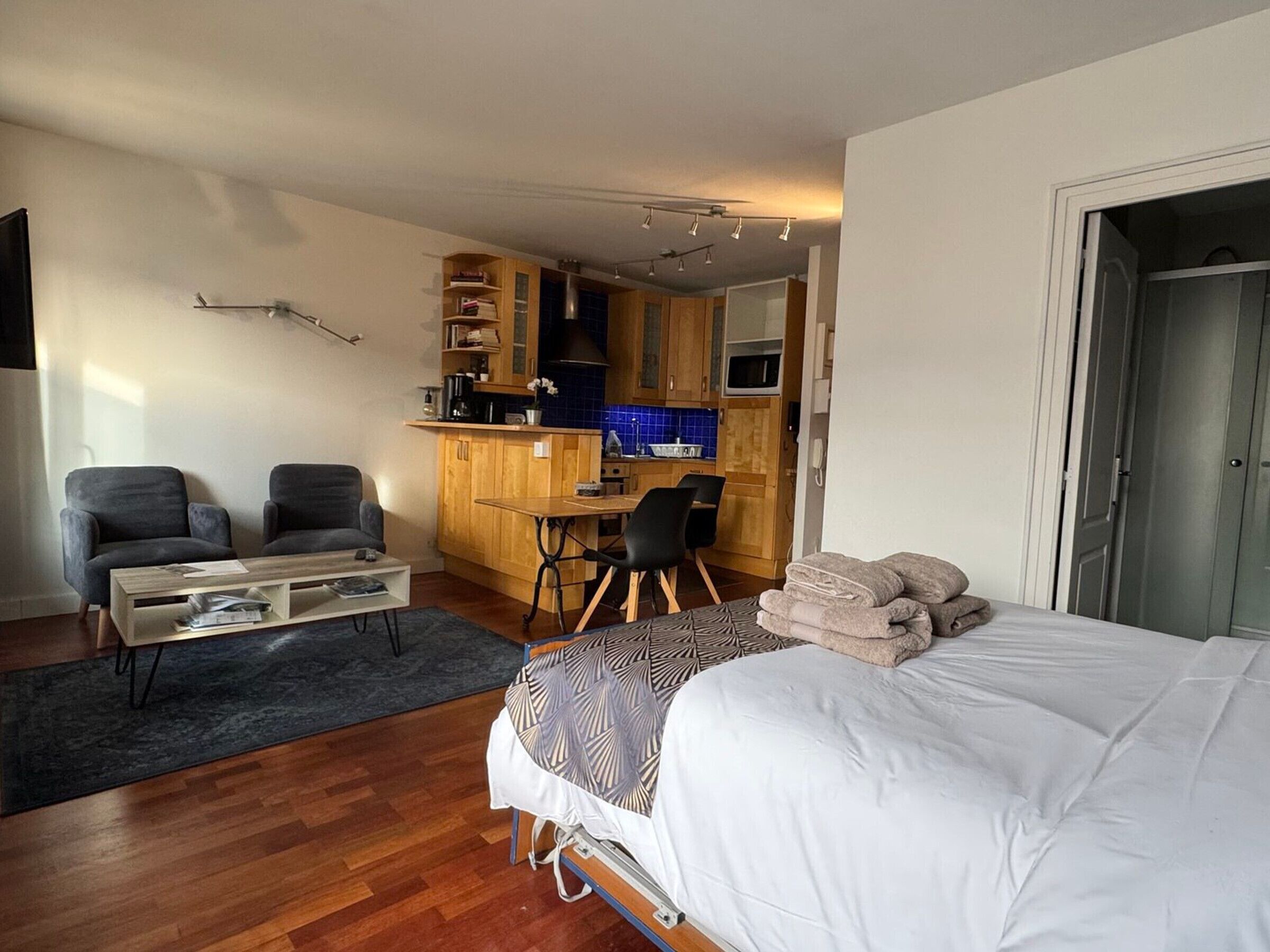 A compact room with a bed, a small desk, two chairs, a coffee table, and a kitchenette.
