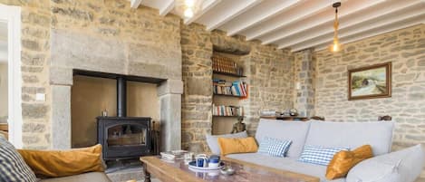 A cozy living room with a stone fireplace, a sofa, a coffee table, and bookshelves.