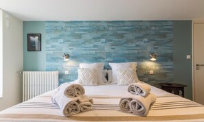 Een hotelkamer met een bed, twee wandlampen, een radiator en een lijst aan de muur.