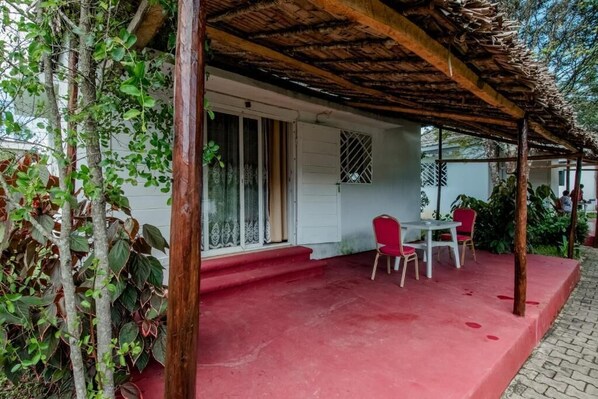 A covered outdoor seating area with a red floor, a white door, and a window with a decorative grille.